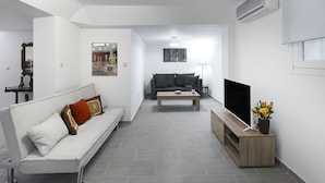A modern living room with a white sofa, a dark sofa, a coffee table, a TV on a wooden stand, and a small table with flowers.