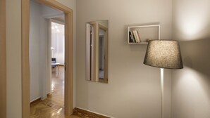A hallway with a wooden floor, a mirror, a bookshelf, and a floor lamp. - Apollonos Amalia Studio - Apollonos Studio (Athens)