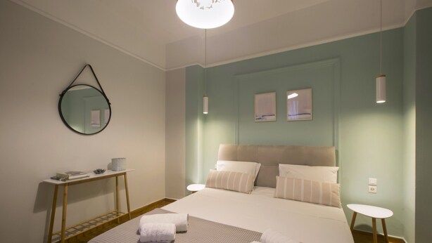 A neatly arranged bedroom with a bed, bedside tables, a hanging mirror, and wall-mounted artwork. - Apollonos Amalia Studio - Apollonos Studio (Athens)