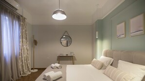 A neatly arranged hotel room with a large bed, a bedside table with a lamp, a mirror on the wall, and a view of the outside through the window. - Apollonos Amalia Studio - Apollonos Studio (Athens)