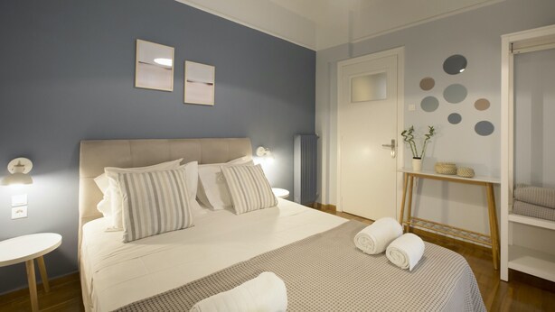 Een netjes ingerichte slaapkamer met een groot bed, nachtkastjes, een klein rond tafeltje en een deur met een spiegel.