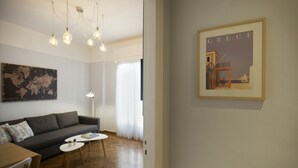 Una sala de estar moderna con un sofá gris, una mesa redonda de centro y un cuadro enmarcado de Grecia en la pared.
