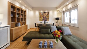 A modern living room with a sofa, a wooden bookshelf, a dining table with chairs, and a painting on the wall. - Karneadou34 · Stylish Kolonaki 2 Bdr apartment (Athens)