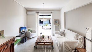 Sala de estar com mesa de centro de madeira, sofás brancos, televisão e vista para o exterior.