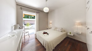 Quarto moderno com uma cama grande, luminárias de cabeceira, uma mesinha e vista para o exterior.