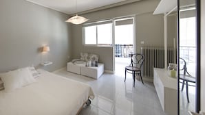 Quarto de hotel moderno com uma cama, sofá, escrivaninha e cadeira. Há uma janela com persianas e um radiador.