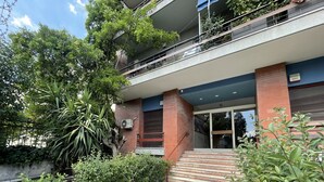 Een meerhoog gebouw met een entree van natuursteen tegels, een trap naar de begane grond en een balkon op de bovenverdieping.