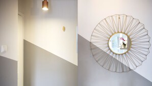 Un intérieur moderne agrémenté d’un grand miroir mural aux motifs géométriques, d’un escalier et d’une suspension lumineuse.