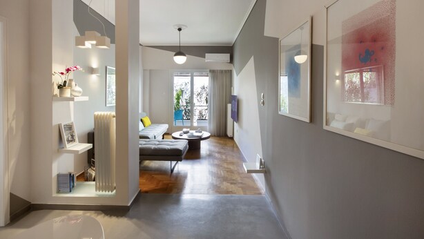 Un intérieur moderne avec un couloir menant à un espace de vie, comprenant un canapé, une table basse et des œuvres d’art accrochées aux murs.