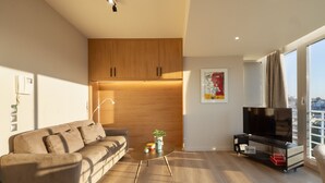 A modern living room with a sofa, a coffee table, a TV, and a large window with a city view. - Ippodamou 25- Acropolis view renovated apartment (Athens)