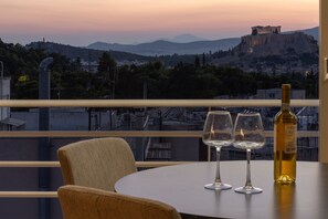 Une table avec deux verres à vin et une bouteille, donnant sur un paysage urbain avec une colline imposante et des ruines antiques.