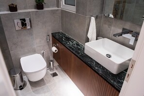 A modern bathroom with a white toilet, a sink with a marble countertop, and a mirror above the sink. - Michalakopoulou94 · Katia Modern Apartment in Athe (Athens)