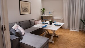 A modern living room with a grey sofa, a white dining table set for two, and a small plant on a shelf.