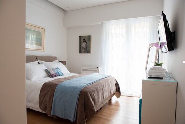 A bedroom with a bed, a bedside table with a plant, a painting on the wall, and a window with curtains. - Michalakopoulou94 · Katia Modern Apartment in Athe (Athens)