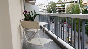 A balcony with a white chair and a small table, overlooking a street with cars and buildings.