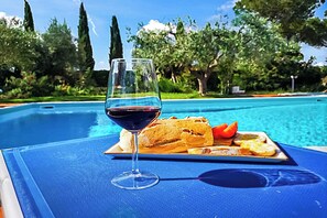 A poolside setting with a glass of red wine, a plate of bread, and a slice of tomato.