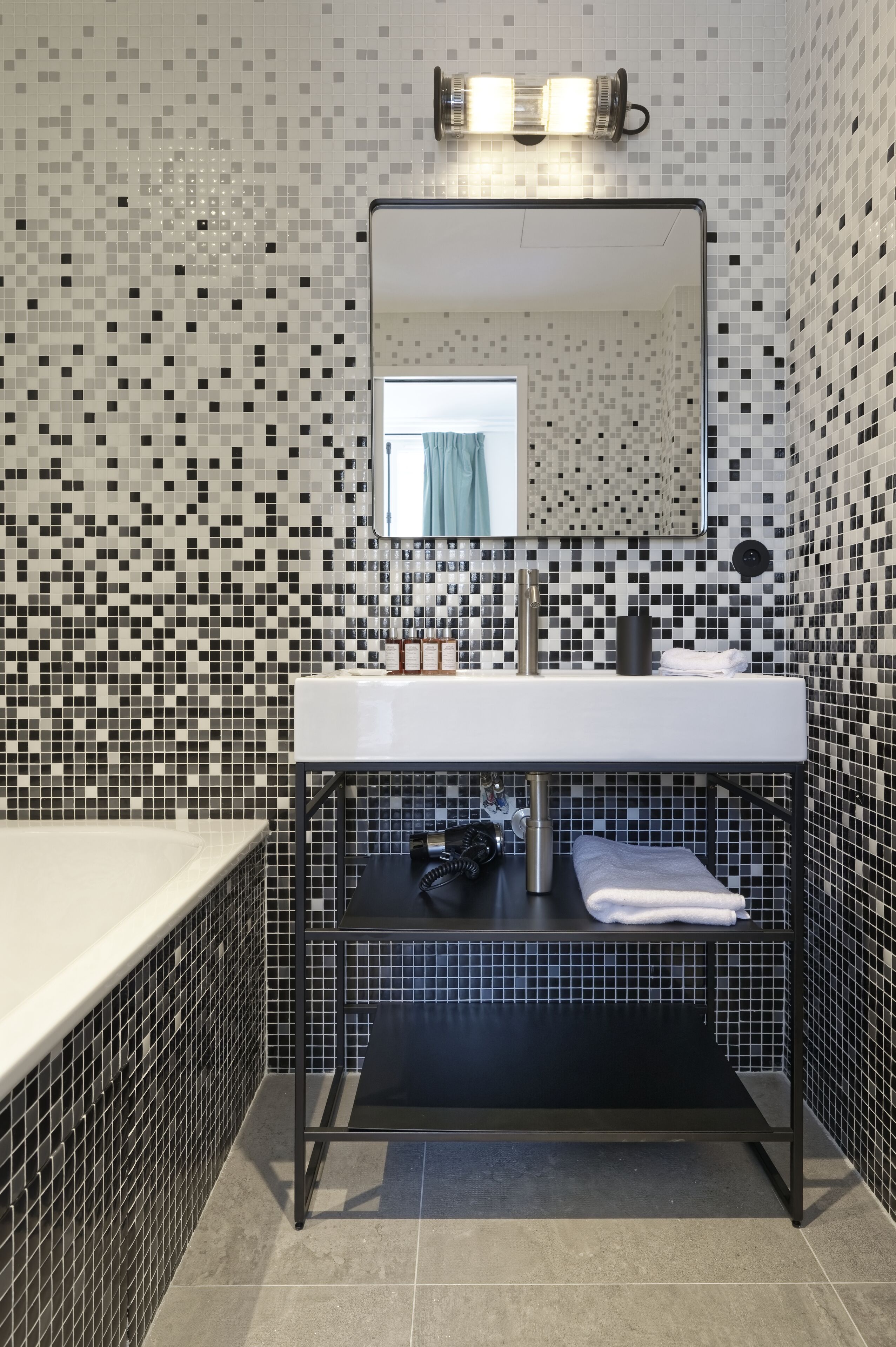 A bathroom with a tiled mosaic wall, a white sink, a black shelf, and a mirror above the sink.