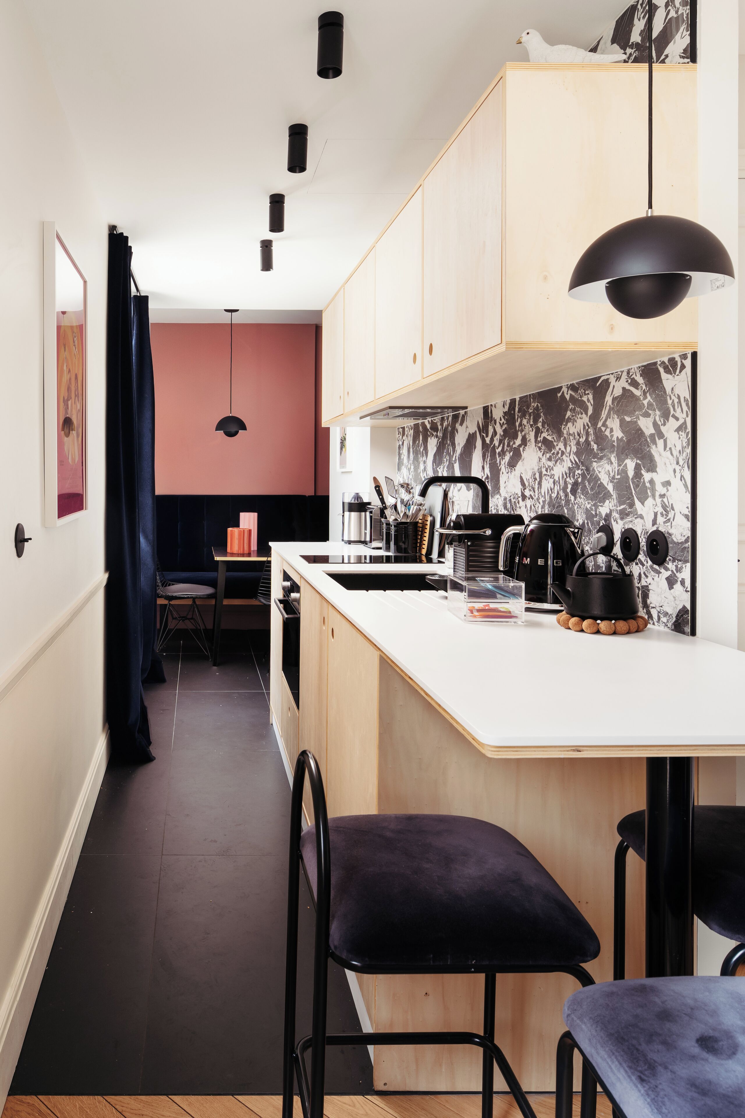 A modern kitchen with a central island, black pendant lighting, and a marble backsplash.