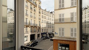 A view from a window overlooking a street with buildings, a car, and a storefront labeled "IMMOBILIER". - My Maison In Paris - Champ de Mars (Paris)