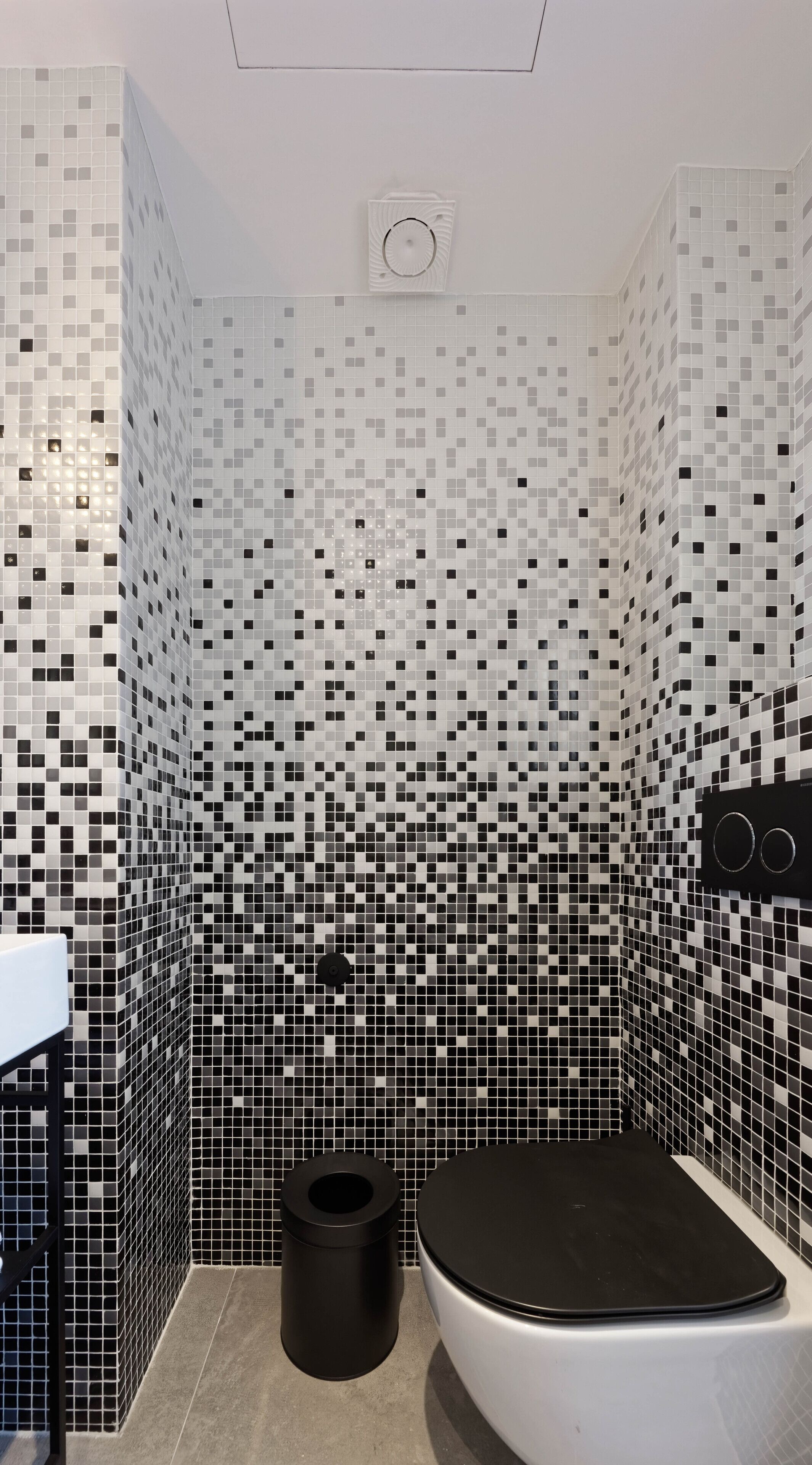Un baño con pared de mosaicos, un inodoro negro y un cubo de basura negro.