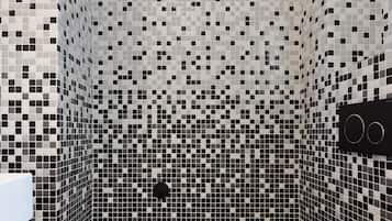 Un baño con pared de mosaicos, un inodoro negro y un cubo de basura negro.