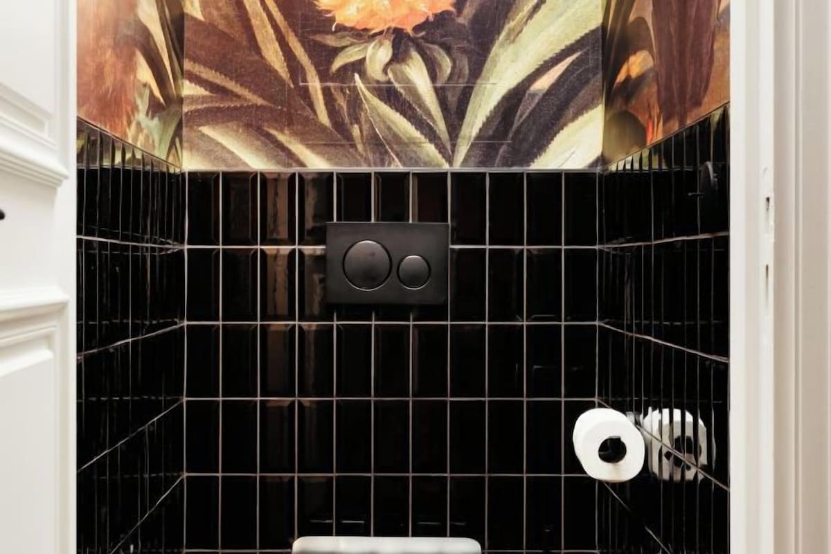 A bathroom with black tiled walls, a toilet, and a shower area.