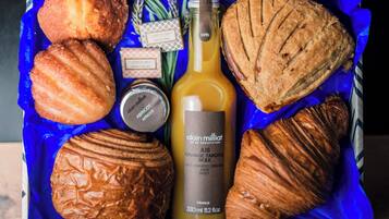 A blue basket containing pastries, a bottle of orange juice, and a jar of apricot jam.