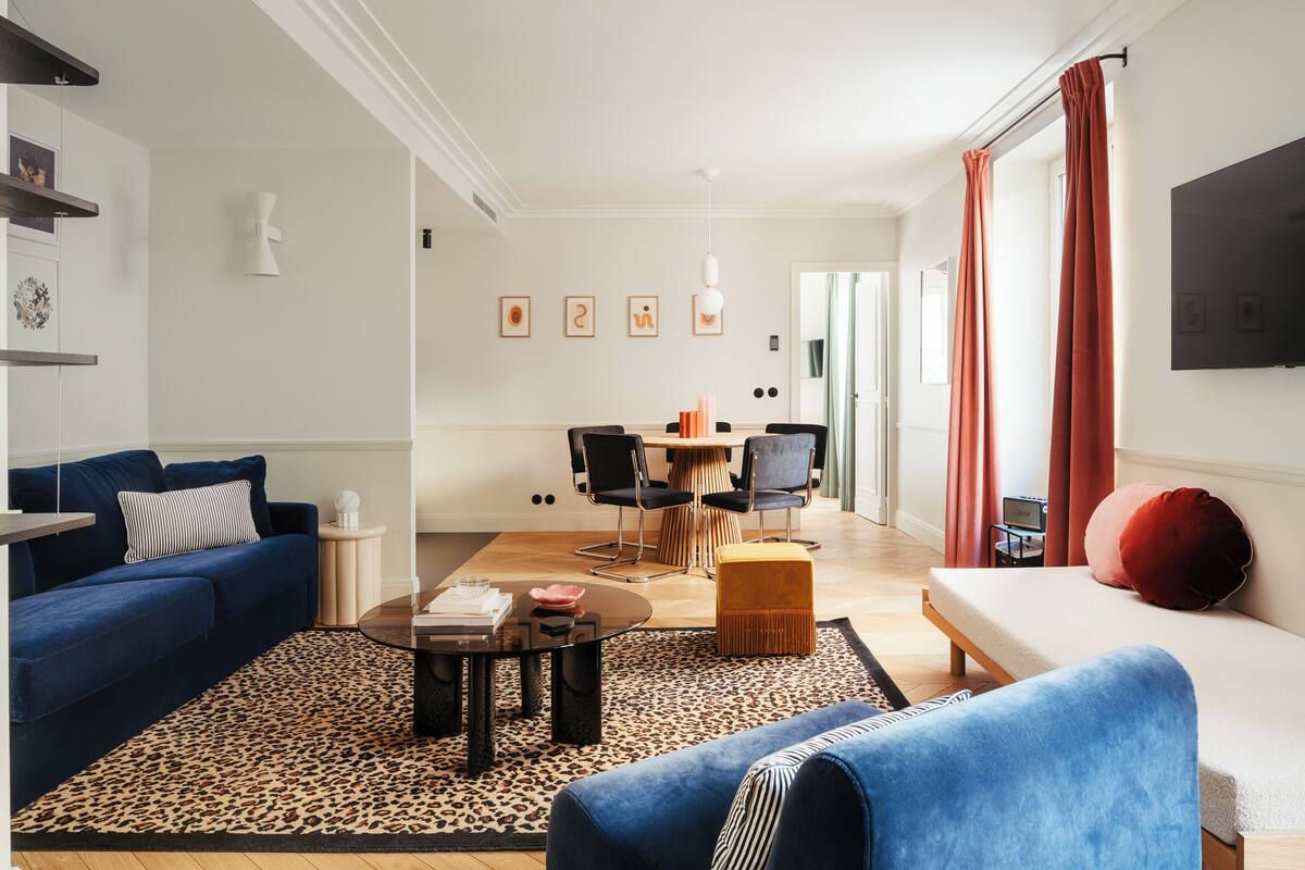 A modern living room with a blue sofa, a coffee table, and a dining area with a wooden table and chairs.