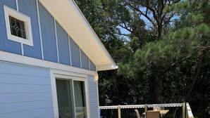 A wooden deck with Adirondack chairs and a table, a blue house with white trim, and a white railing. - D110- Large Private Saltwater Pool, 3 Bedrooms and Only 600 Yards to Beach!! (Duck)