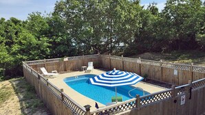A rectangular swimming pool with a blue and white striped umbrella, surrounded by a wooden fence with a lattice top. - D110- Large Private Saltwater Pool, 3 Bedrooms and Only 600 Yards to Beach!! (Duck)