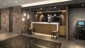 Een modern receptiegebied met een stenen muur, een houten receptiebalie, twee barkrukken, een digitale kiosk en een brandmelder.