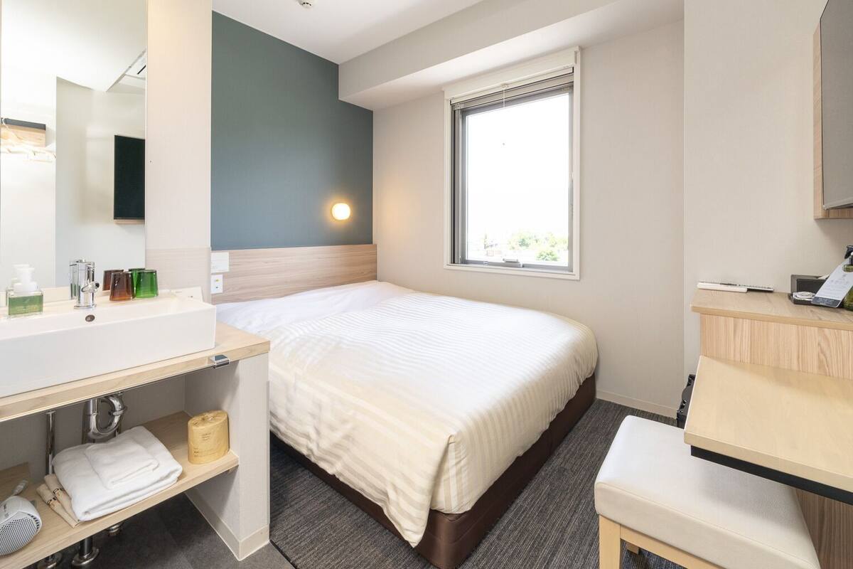Een hotelkamer met een bed, een bureau, een spiegel, een raam en een badkamergedeelte.