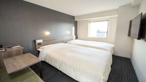 Een hotelkamer met twee bedden, een bureau en een raam met uitzicht op de stad.