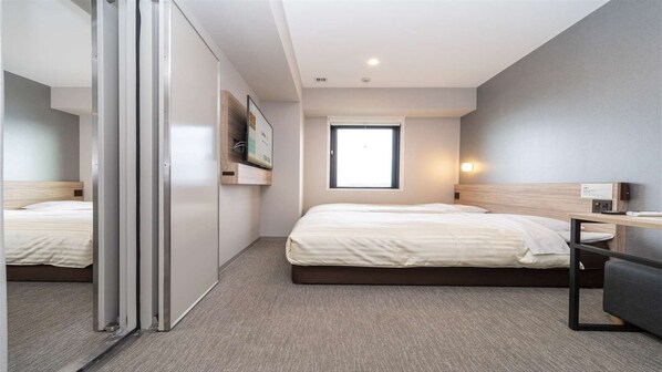A hotel room with two beds, a desk, a window, and a sliding door.