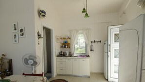 Una cocina pequeña con armarios blancos, una ventana con cortinas, un ventilador y un refrigerador.