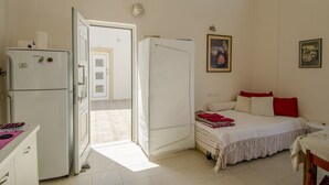 Un dormitorio con una cama, una mesita, una silla, un armario y un refrigerador blanco.