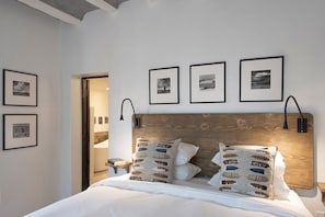 Un dormitorio con cabecera de madera, ropa de cama blanca y varias fotografías enmarcadas en la pared.