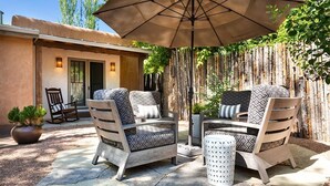 Eine Terrasse im Freien mit zwei Holzstühlen, einem Tisch, einem Sonnenschirm und einem Blumentopf.