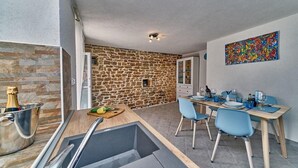 A modern kitchen with a stone wall, a dining area with blue chairs, and a colorful abstract painting on the wall. - Villa with Private Jacuzzi (Šolta)