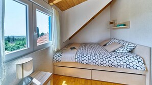A bedroom with a sloped ceiling, a bed with patterned bedding, a bedside table, and a window with a view of greenery. - Villa with Private Jacuzzi (Šolta)