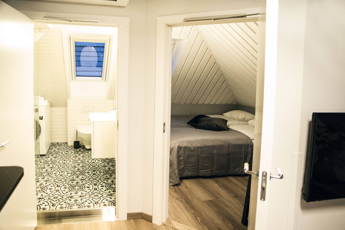 A bedroom with a sloped ceiling, a bed, and a small window.