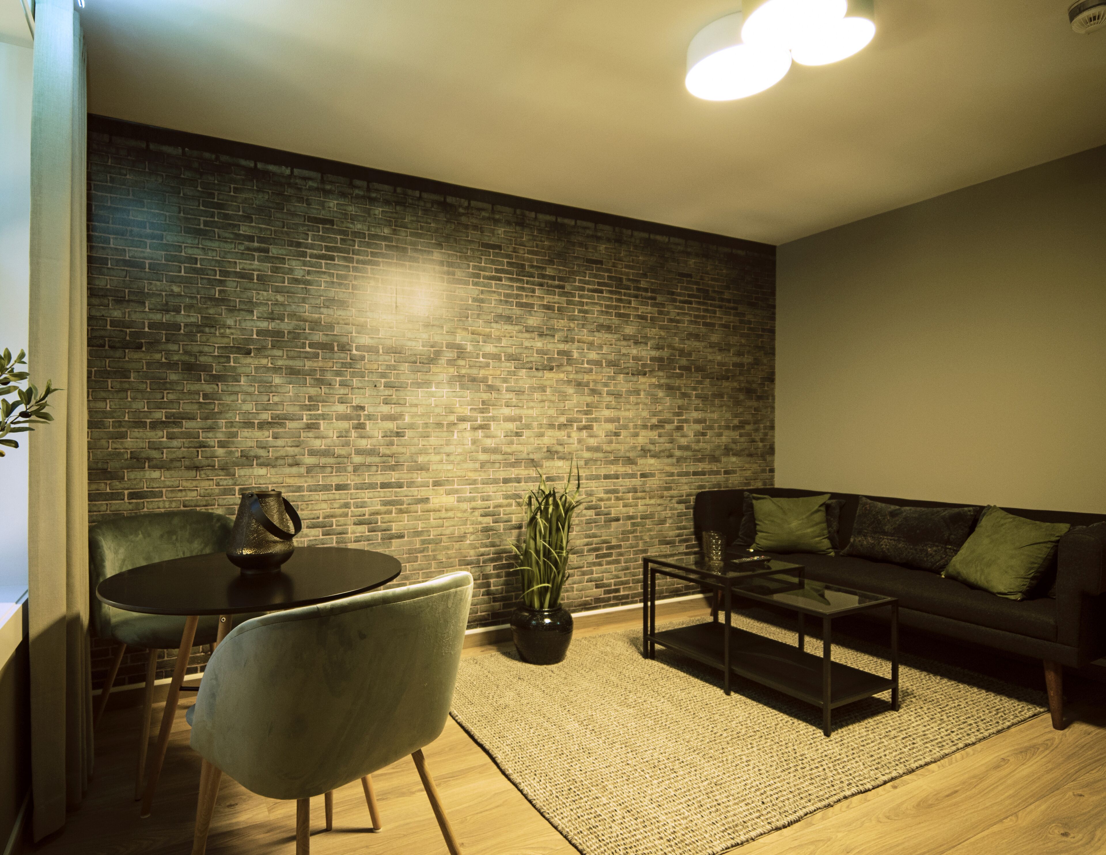 A modern living room with a brick wall, a round table with chairs, a sofa, and a coffee table.