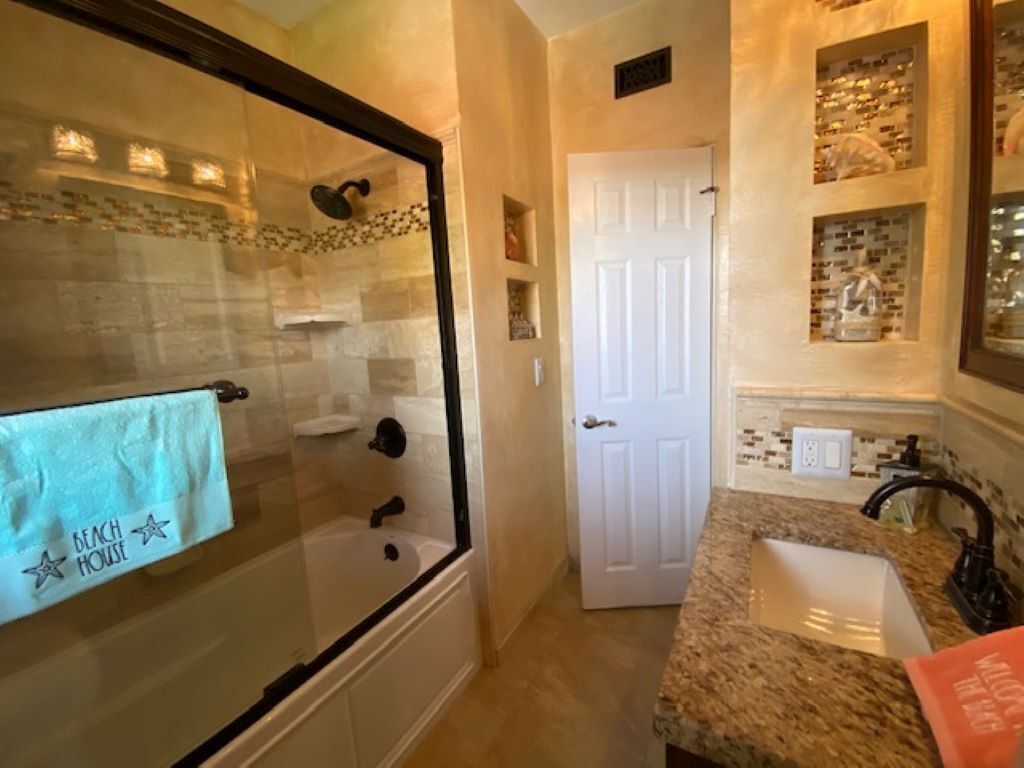 A bathroom with a glass-enclosed shower, a white door, and a granite countertop with a sink.