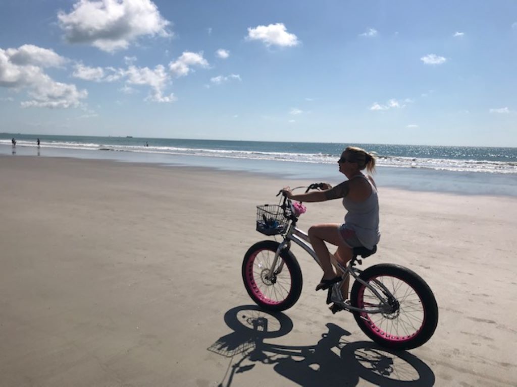 Una persona montando en bicicleta sobre una playa arenosa con el océano al fondo.