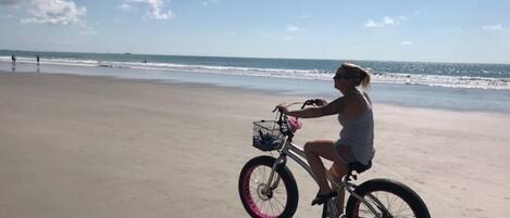 Una persona montando en bicicleta sobre una playa arenosa con el océano al fondo.