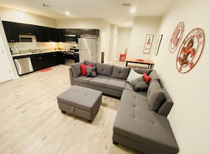 Relax in this stylish living space with a grey sofa, matching ottoman, and armchair. Enjoy a fully equipped kitchen with black cabinets and stainless steel appliances.
