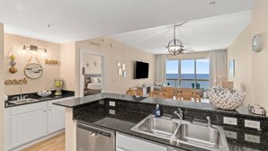 A modern kitchen with a large island, a dining area with a view, and a living space with a TV and artwork. - Calypso TOWER 1! Gulf Front! No Obstructions! (Panama City Beach)
