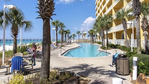 A pool area with lounge chairs and palm trees, surrounded by a building with balconies. - Calypso TOWER 1! Gulf Front! No Obstructions! (Panama City Beach)