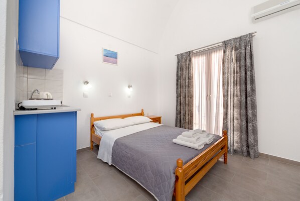 A bedroom with a bed, a blue wardrobe, a small kitchenette, and a window with curtains.