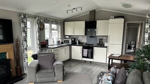 A modern kitchen with white cabinets, a microwave, stove, and sink. There is a grey sofa and a patterned rug in the living area. - Beautiful and Tranquil Lakeside Lodge - Sleeps 5 (Northampton)